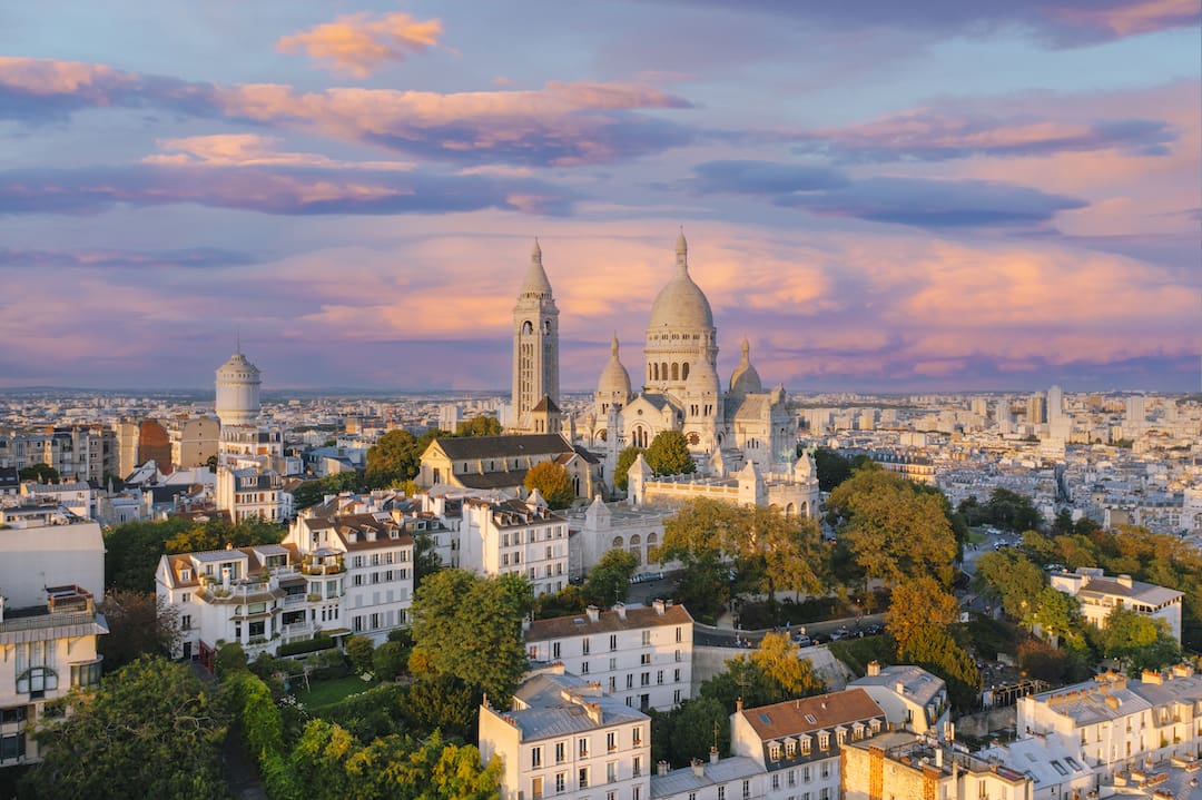 Panoramisk udsigt over Montmartre i Paris ved solnedgang, med den ikoniske Sacré-Cœur basilika, der dominerer bybilledet