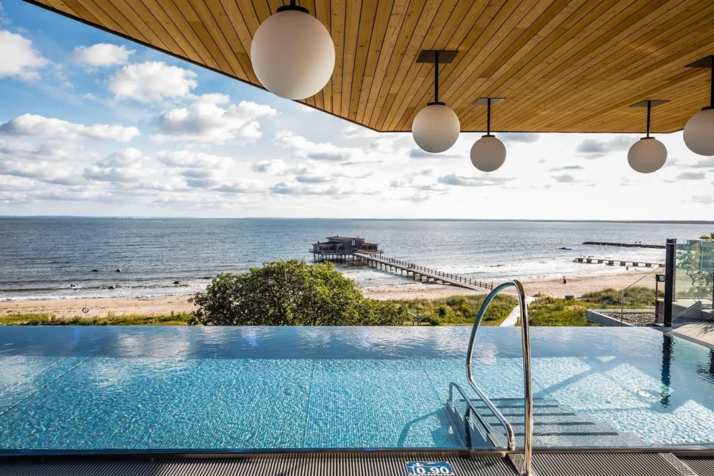 Infinity poolen på Hotel Skansen med en spektakulær udsigt over havet og en badebro, der strækker sig ud i vandet. Poolen er beliggende på en terrasse med moderne lamper hængende fra loftet og tilbyder gæsterne en luksuriøs og afslappende oplevelse med panoramaudsigt over stranden og det åbne hav. Dette er det perfekte sted at nyde solnedgangen og den friske havluft, mens man slapper af i vandet.