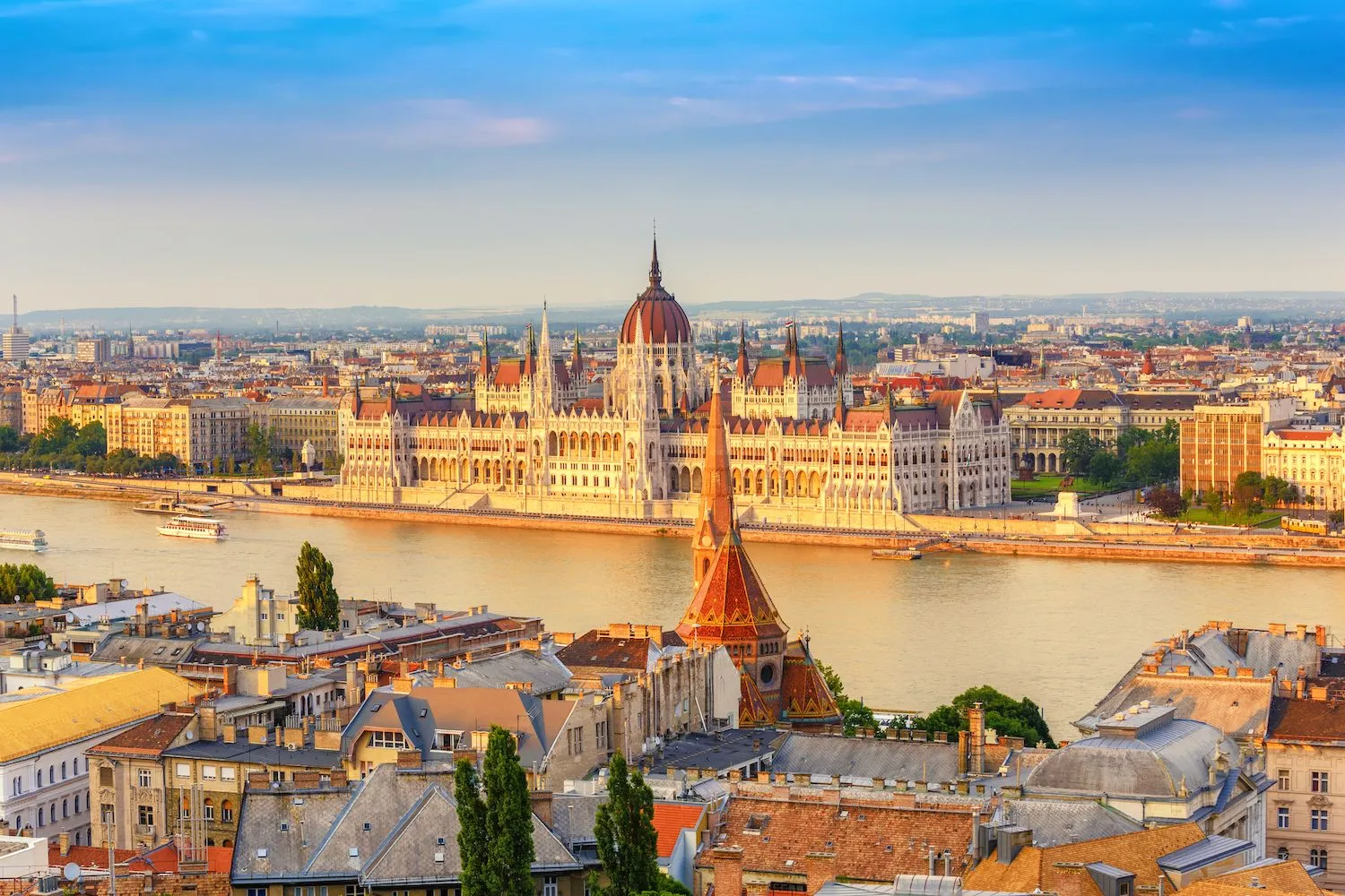 Udsigt over Budapest med det imponerende parlament ved bredden af Donau-floden badet i gyldent sollys. Den perfekte destination for en afslappende og kulturel miniferie i Europa, hvor historie og smuk arkitektur mødes i hjertet af byen.