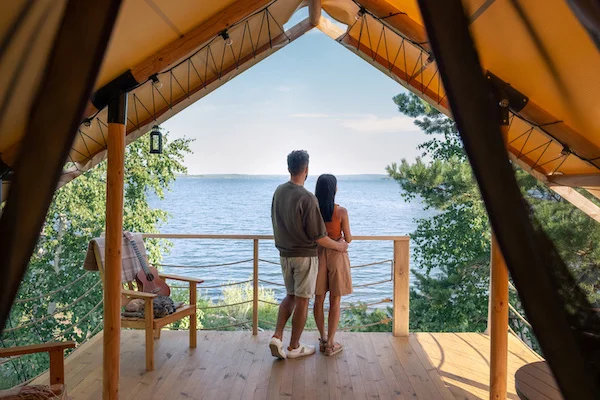 Par nyder en betagende udsigt over søen fra en luksuriøs glamping-hytte med åben terrasse.