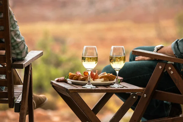 To glas hvidvin og snacks på et bord under en afslappende glamping-oplevelse i naturskønne omgivelser.